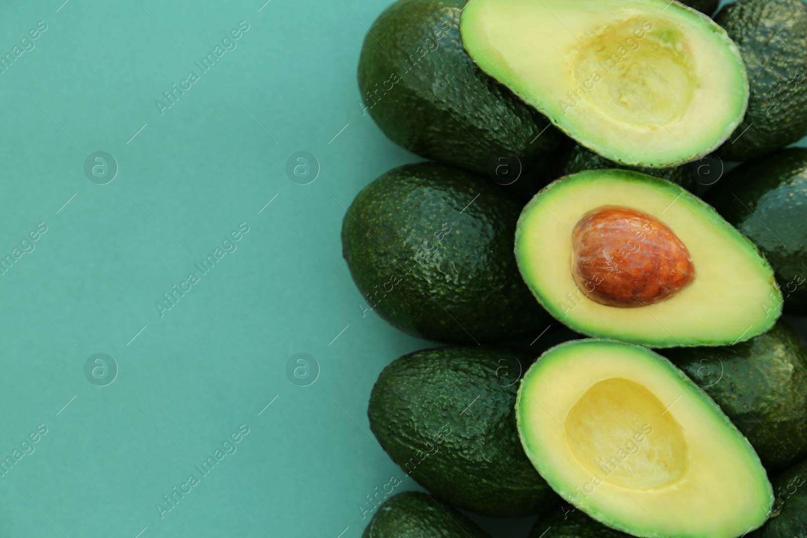 Photo of Tasty whole and cut avocados on turquoise background, top view. Space for text