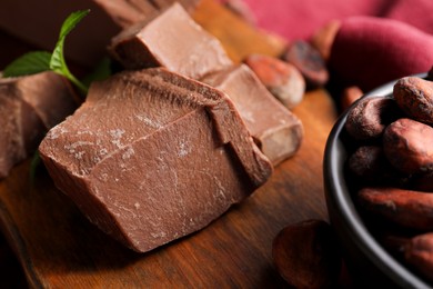 Photo of Pieces of tasty milk chocolate and cocoa beans on wooden table, closeup