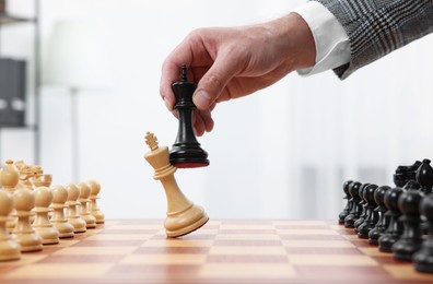 Photo of Man with king game piece playing chess at checkerboard indoors, closeup