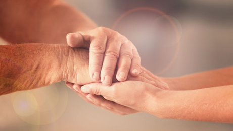 Image of Volunteer and elderly woman holding hands in sunlit room, closeup