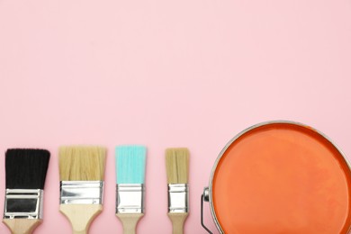 Photo of Bucket of orange paint and brushes on pink background, flat lay. Space for text