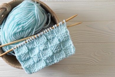 Photo of Soft turquoise yarn, knitting and needles on white wooden table, top view. Space for text