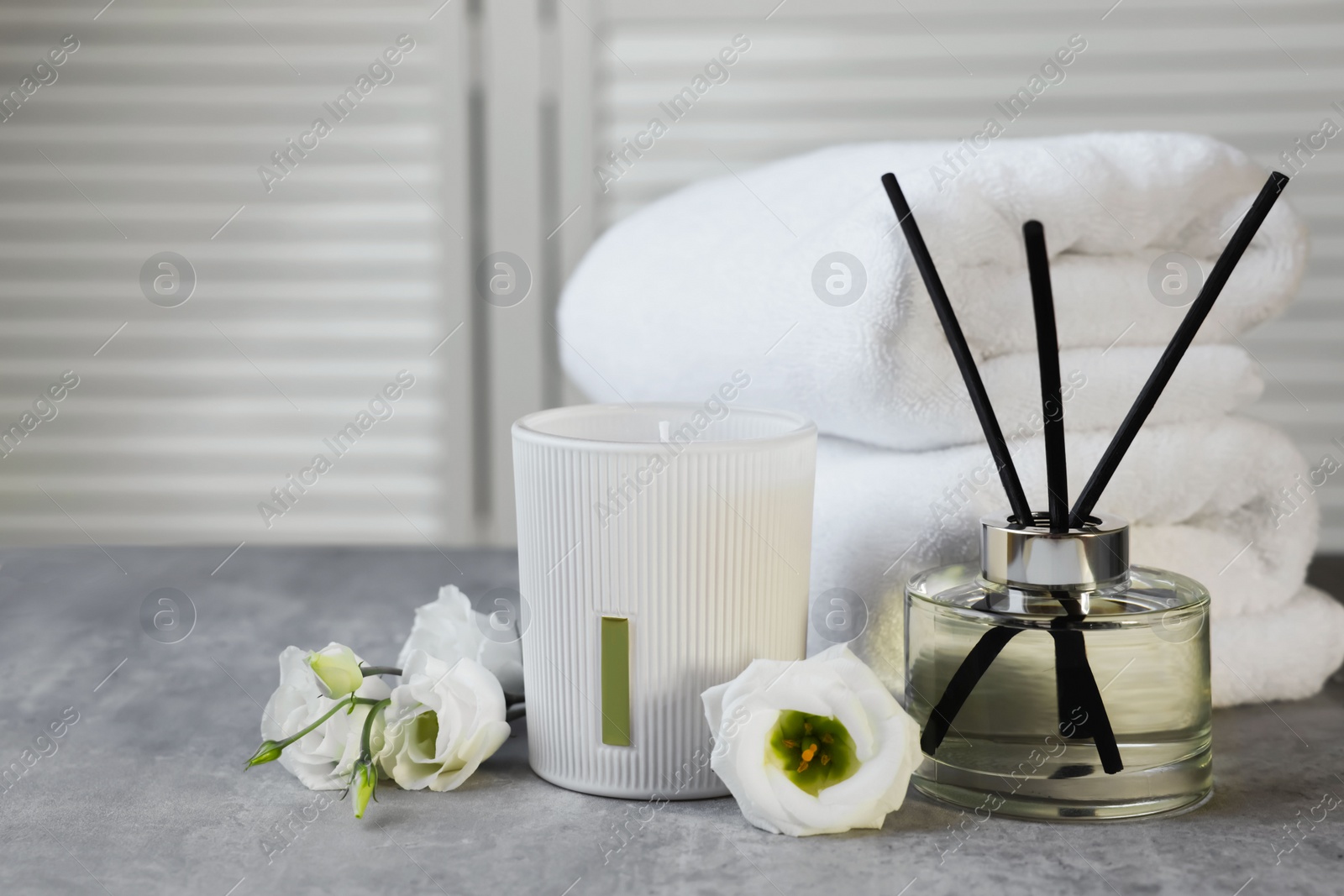 Photo of Reed diffuser, scented candle, flowers and folded towels on gray marble table