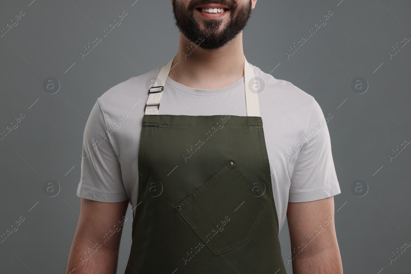 Photo of Smiling man in kitchen apron on grey background, closeup. Mockup for design