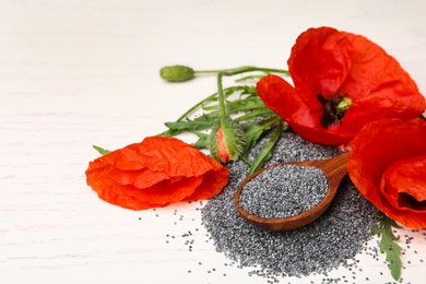 Spoon of poppy seeds and flowers on white wooden table, space for text