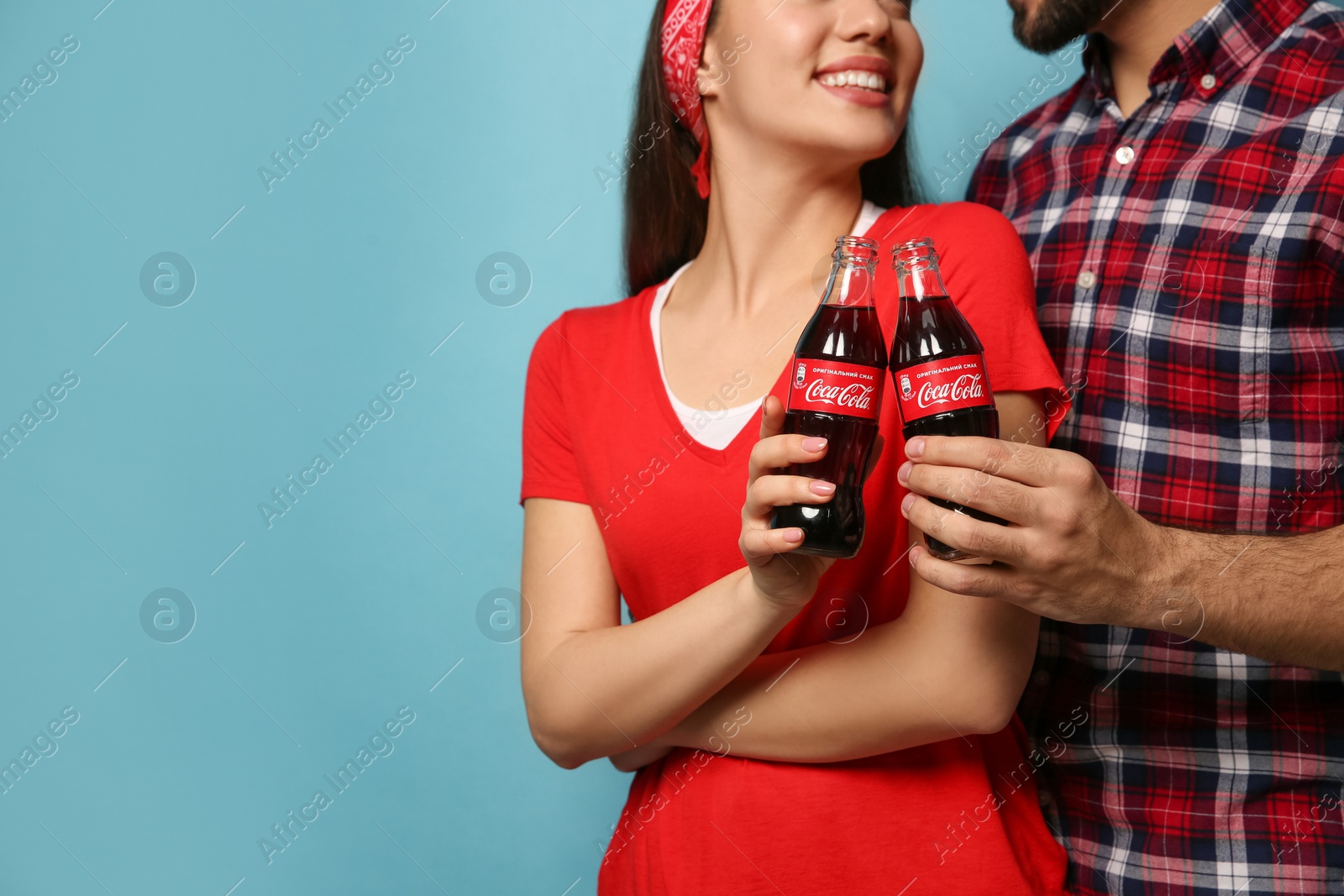 Photo of MYKOLAIV, UKRAINE - JANUARY 27, 2021: Young couple holding bottles of Coca-Cola on light blue background, closeup. Space for text