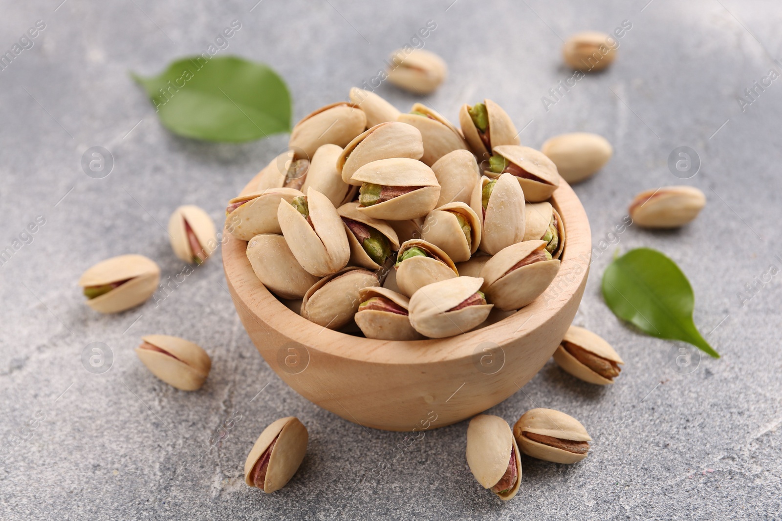 Photo of Delicious pistachios in bowl on grey textured table