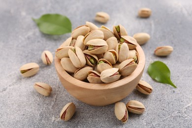 Delicious pistachios in bowl on grey textured table