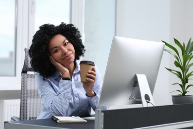 Young woman with cup of drink working on computer in office