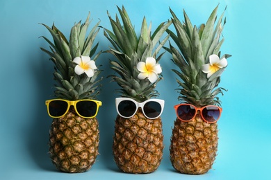 Photo of Funny pineapples with sunglasses and plumeria flowers on light blue background. Creative concept