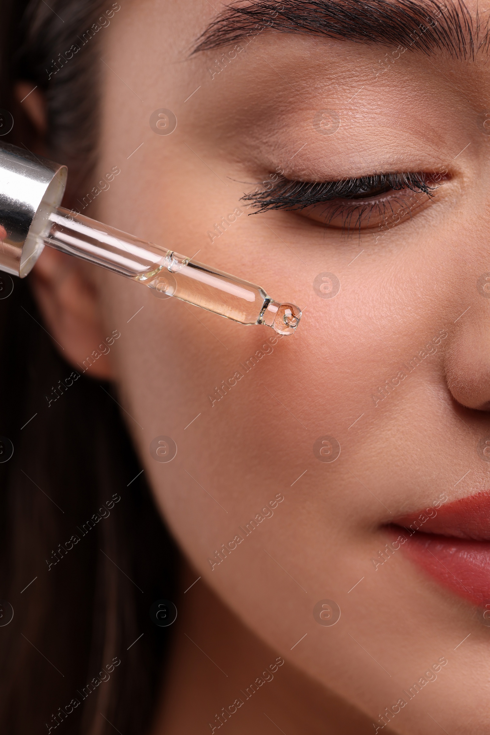 Photo of Young woman applying essential oil onto face, closeup