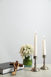 Church candles, wooden cross, rosary beads, Bible and flowers on marble table. Space for text