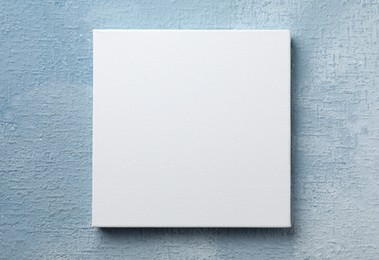 Blank canvas hanging on light blue wall, space for text