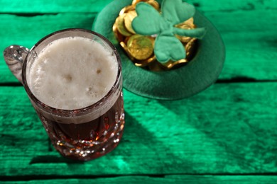 St. Patrick's day. Beer, leprechaun hat with gold and decorative clover leaf on green wooden table. Space for text