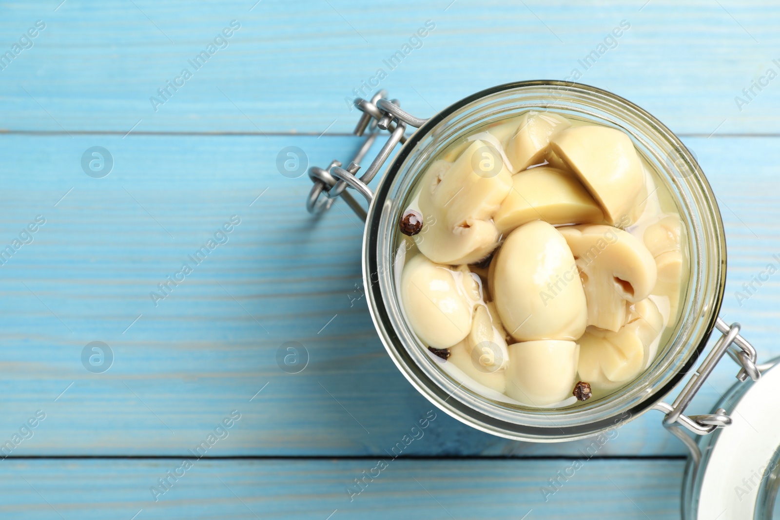 Photo of Delicious marinated mushrooms in glass jar on light blue wooden table, top view