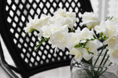 Photo of Beautiful white freesia flowers in vase on armchair, closeup