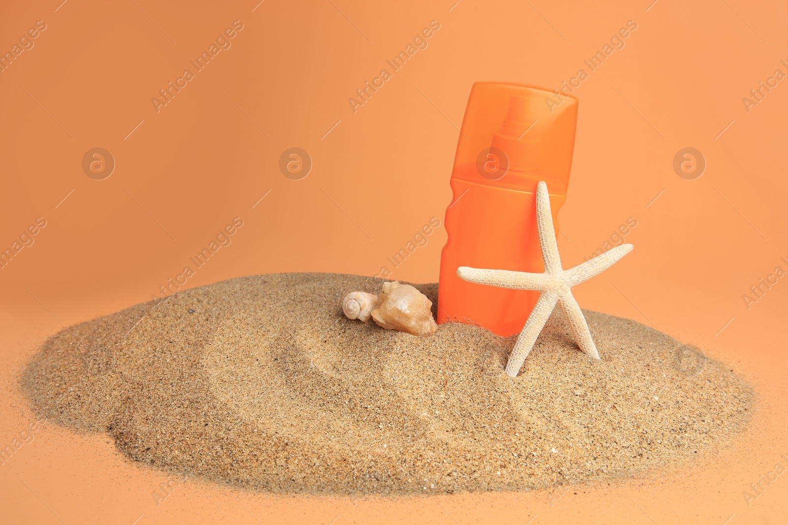 Photo of Sand with bottle of sunscreen, starfish and seashells against orange background. Sun protection