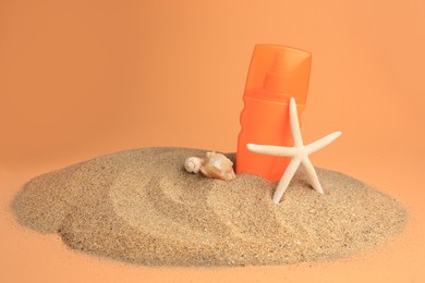 Photo of Sand with bottle of sunscreen, starfish and seashells against orange background. Sun protection