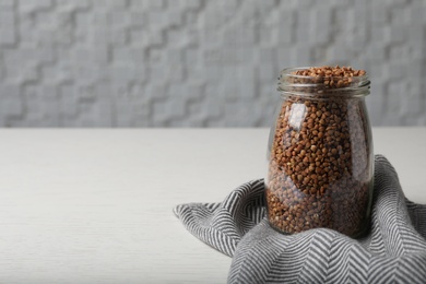 Uncooked buckwheat in glass jar on table. Space for text