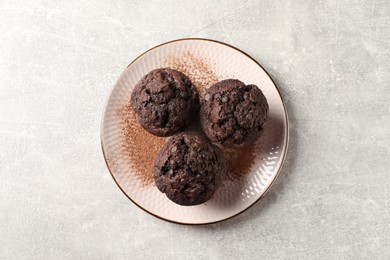 Delicious chocolate muffins and cacao powder on light grey table, top view