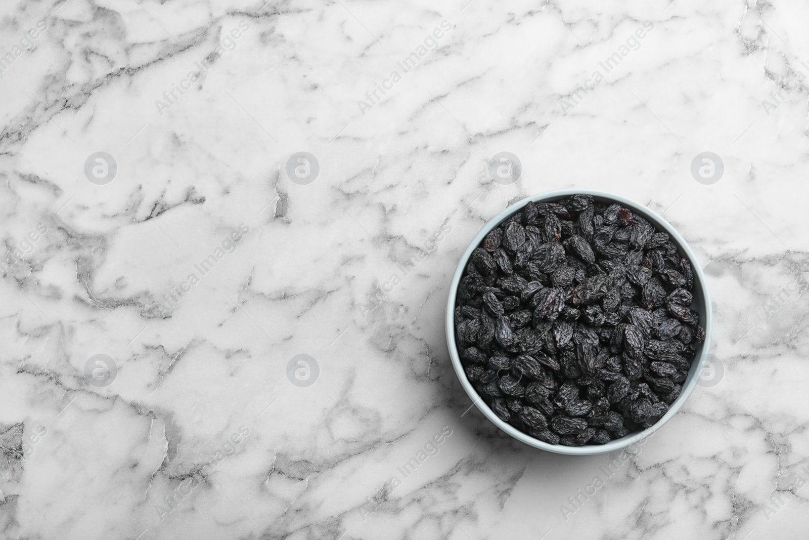 Photo of Bowl with raisins and space for text on marble background, top view. Dried fruit as healthy snack