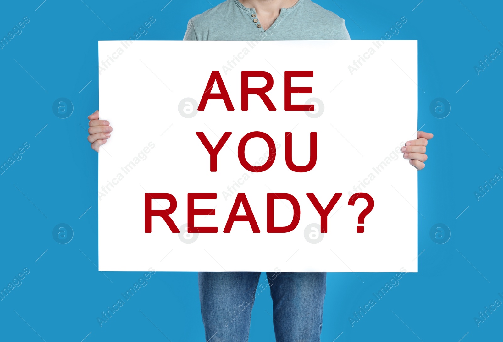 Image of Man holding poster with text Are You Ready? on blue background, closeup