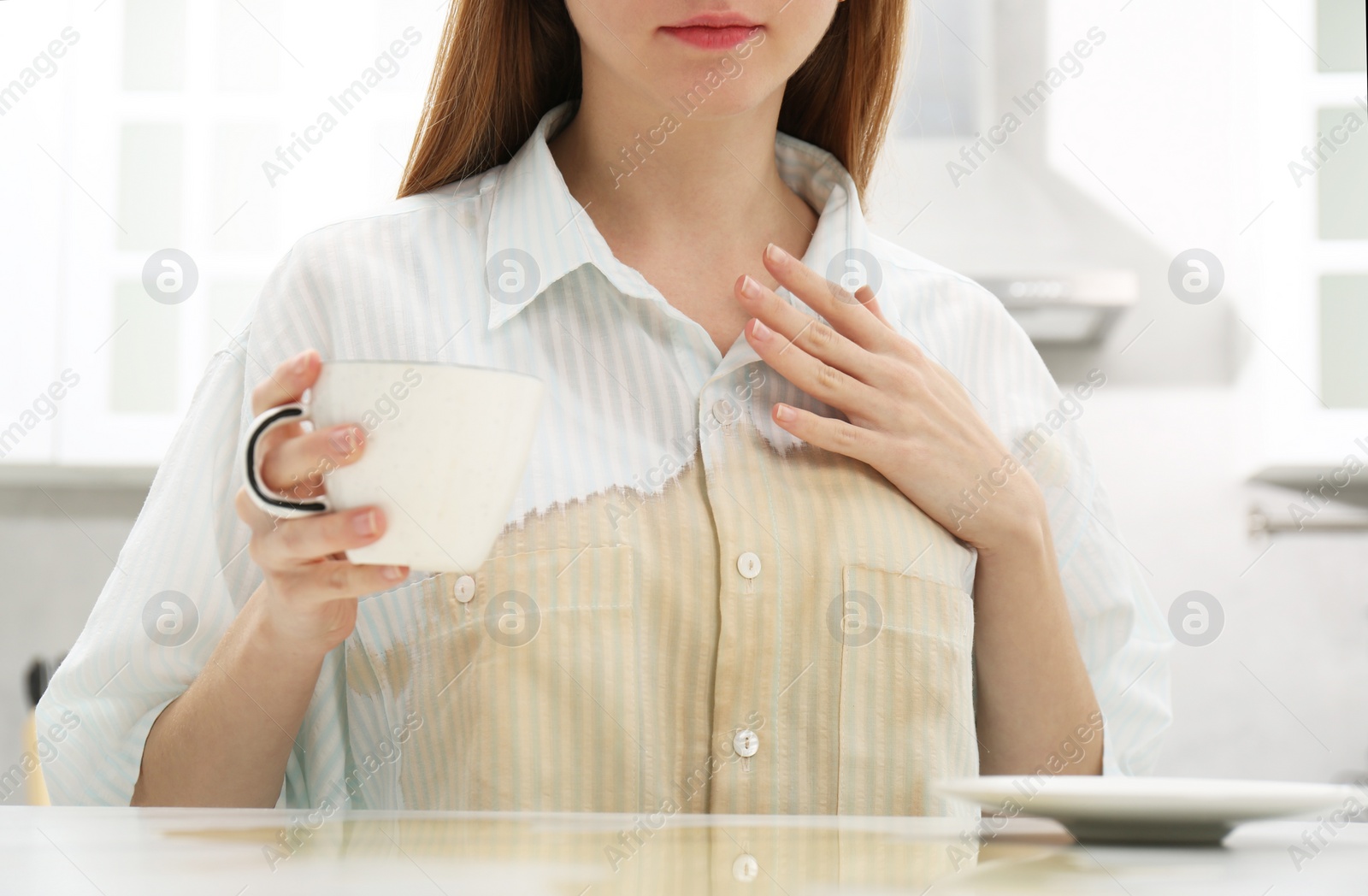 Photo of Woman with spilled coffee over her shirt at table in kitchen, closeup