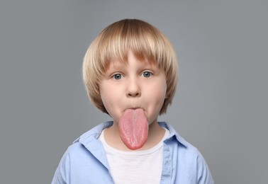 Image of Portrait of cute boy showing long tongue on grey background