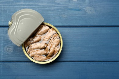 Open tin can of sprats on blue wooden table, top view. Space for text