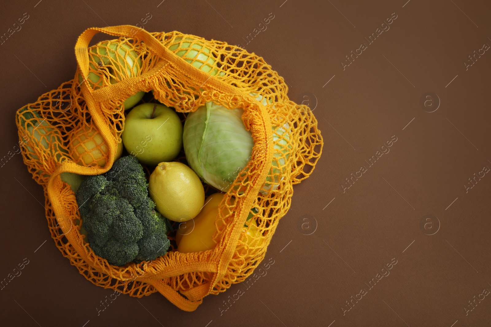 Photo of Net bag with fruits and vegetables on brown background, top view. Space for text