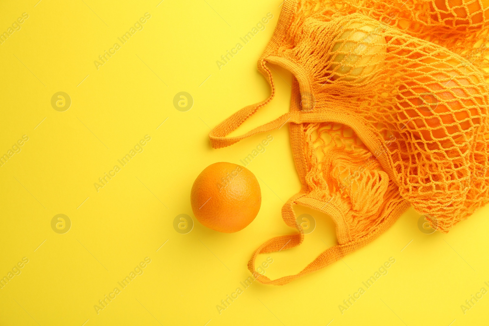 Photo of String bag with fresh oranges on yellow background, top view. Space for text