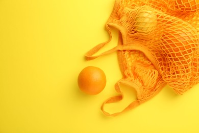 Photo of String bag with fresh oranges on yellow background, top view. Space for text