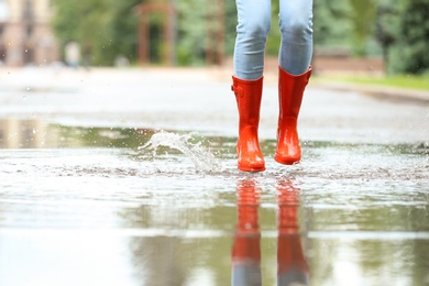 Photo of Woman with red rubber boots jumping in puddle, closeup. Rainy weather