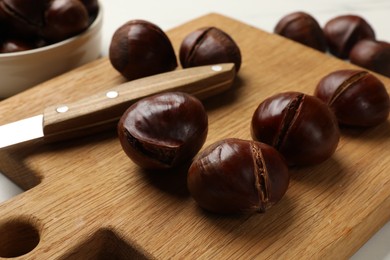Photo of Roasted edible sweet chestnuts and knife on white table, closeup
