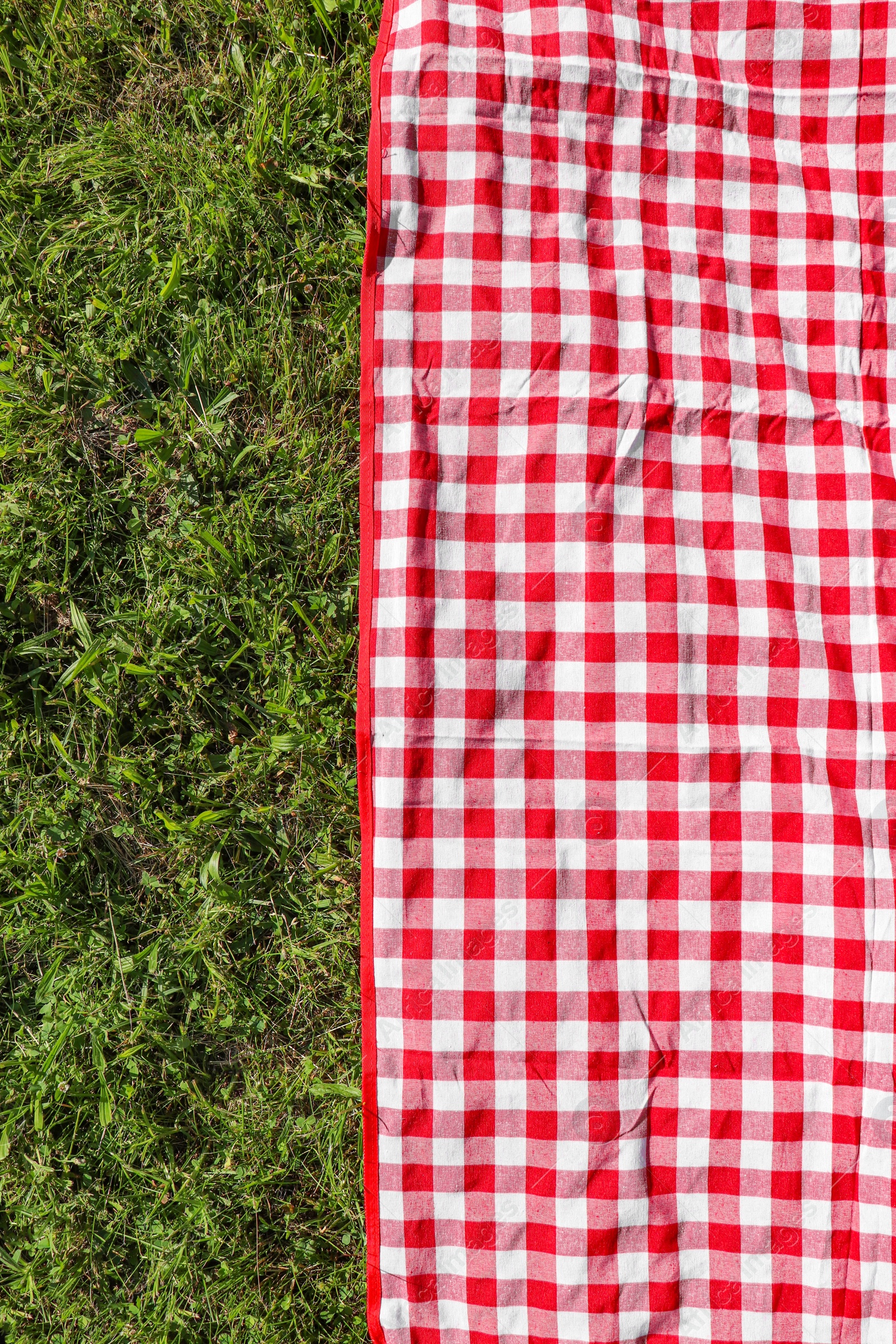 Photo of Checkered picnic tablecloth on fresh green grass, top view. Space for text