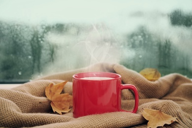 Image of Cup of delicious hot drink, leaves and sweater on window sill
