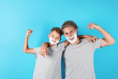 Father and son with shaving foam on faces against color background