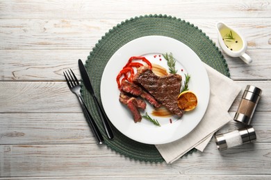 Photo of Delicious grilled beef steak with pepper and spices served on light wooden table, flat lay