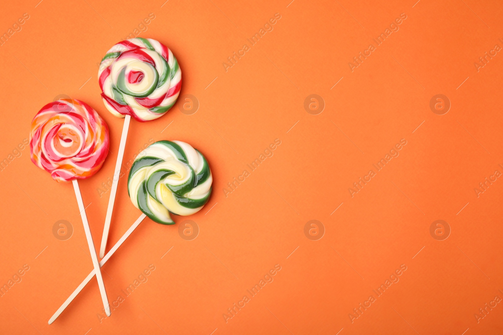 Photo of Colorful lollipops on orange background, flat lay. Space for text