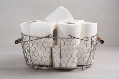 Photo of Soft toilet paper rolls in metal basket on white wooden table, closeup