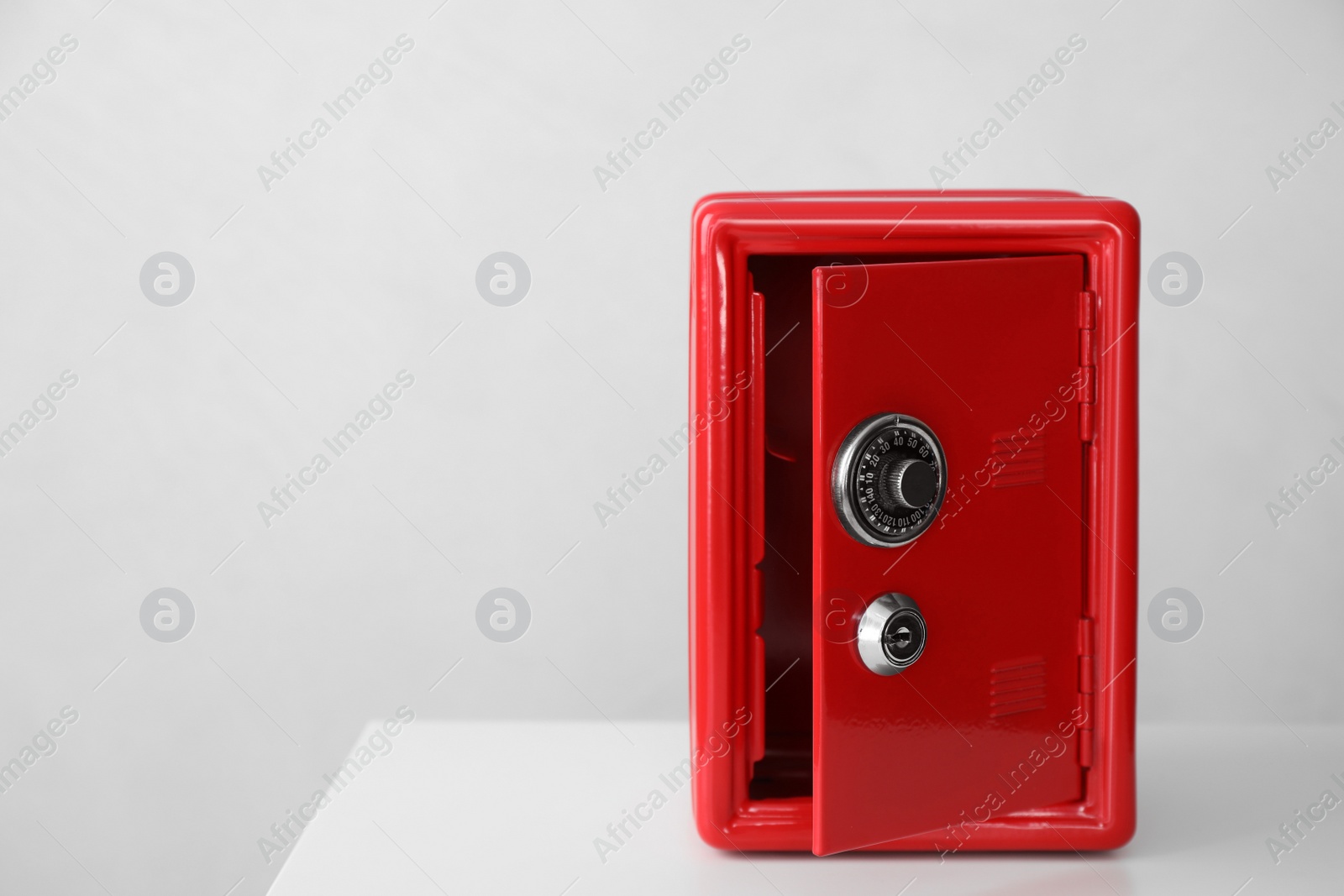 Photo of Red steel safe on white table against light background. Space for text
