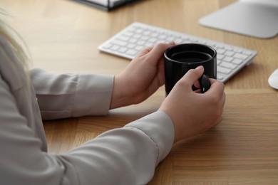 Photo of Woman with black ceramic mug at workplace, closeup