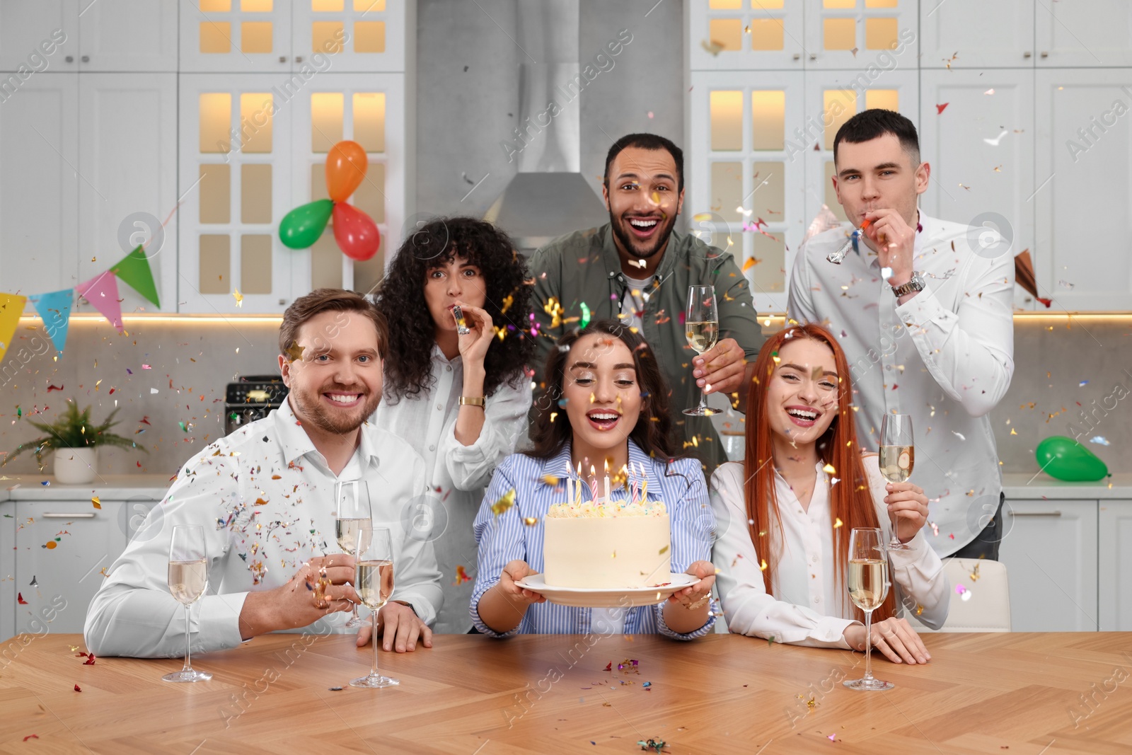 Photo of Happy friends with tasty cake celebrating birthday in kitchen