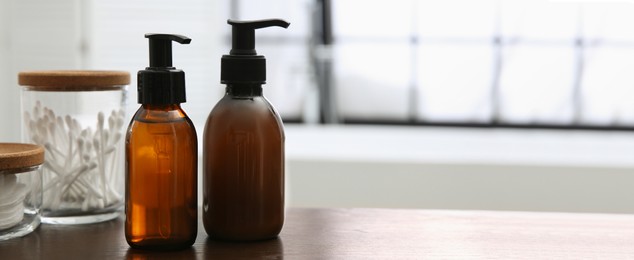 Dispensers of liquid soap on wooden table in bathroom, space for text. Banner design