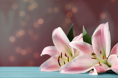 Photo of Beautiful pink lily flowers on turquoise table against blurred lights, space for text
