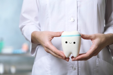 Dentist holding model of tooth with cute face in clinic, closeup view. Space for text