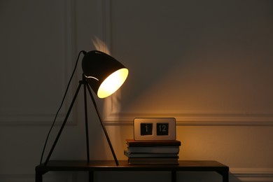 Photo of Wooden table with books, clock and modern lamp near beige wall, space for text. Interior element