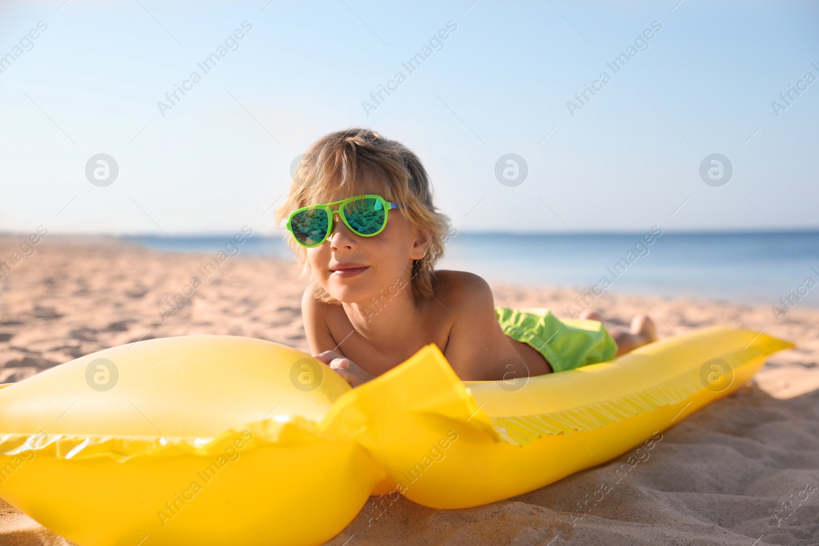 Photo of Cute little child with inflatable mattress lying at sandy beach on sunny day