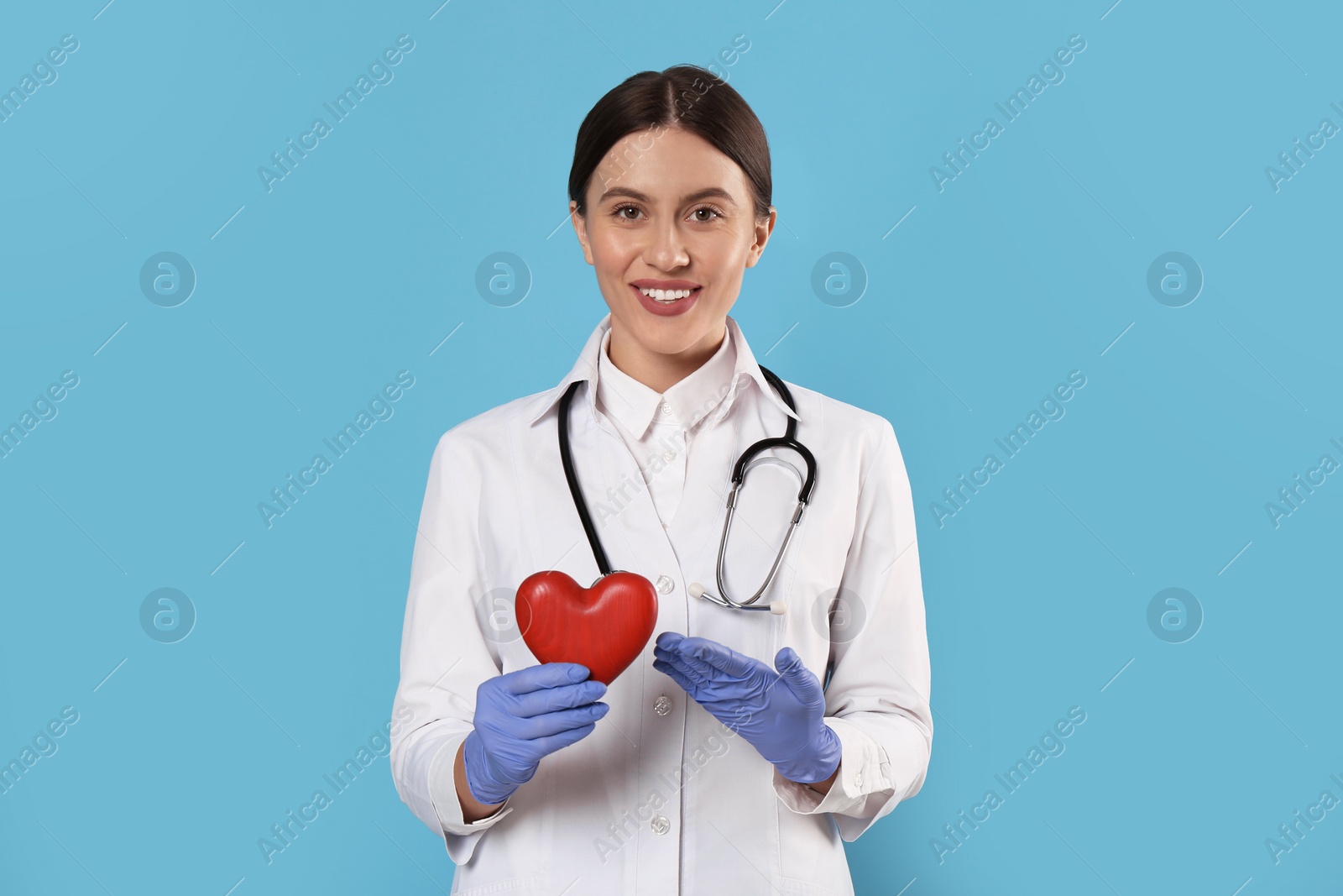 Photo of Doctor with stethoscope and red heart on light blue background. Cardiology concept