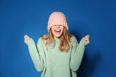 Happy young woman wearing warm sweater and knitted hat on blue background